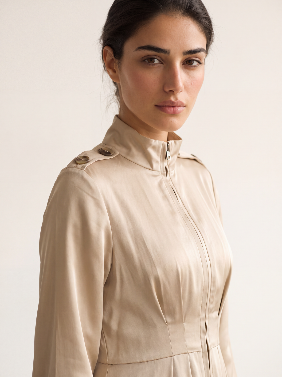 Close-up of a model wearing a light khaki satin utility maxi dress, highlighting the stand collar, front half-zip, and shoulder epaulet details.